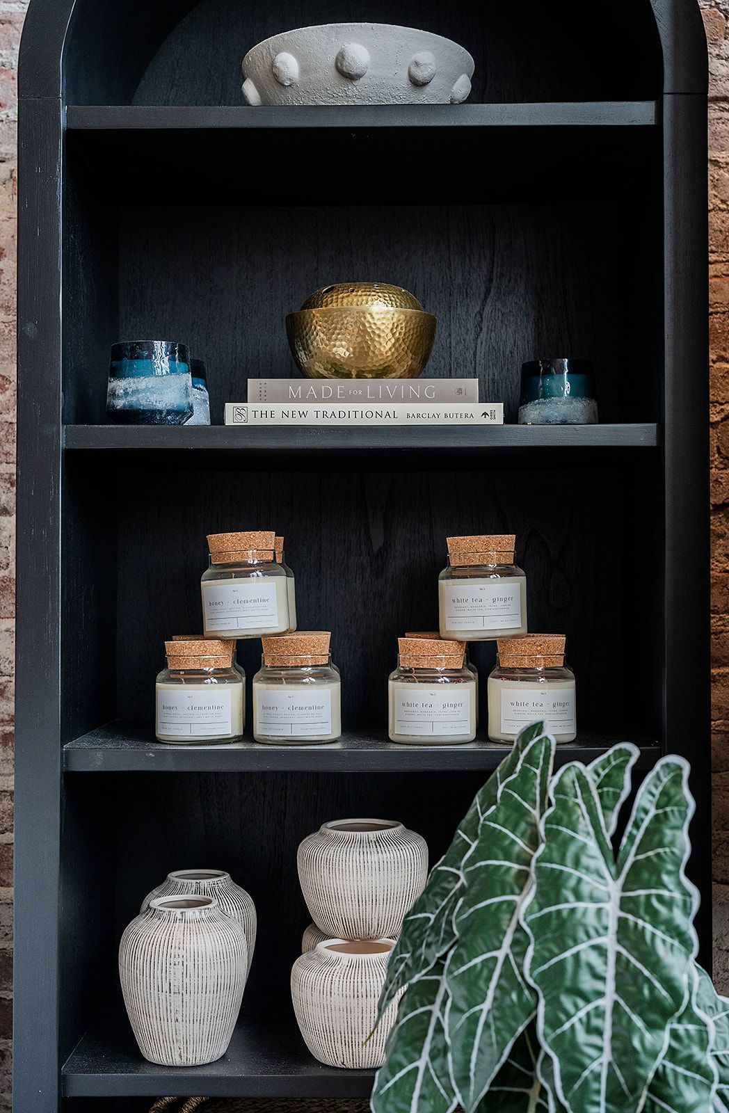 A shelf with candles , vases , and a plant on it.