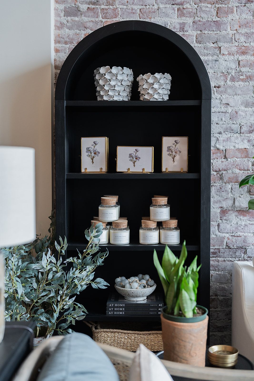 A living room with a black bookshelf filled with candles and potted plants.