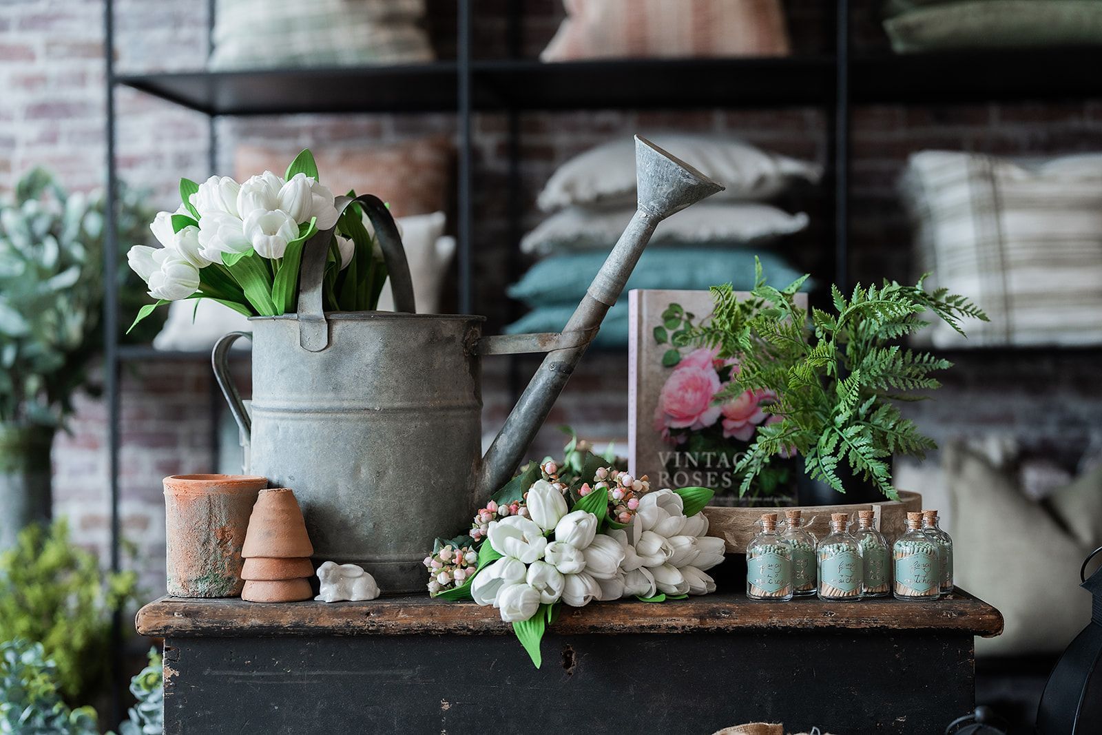 A watering can and flowers are on a table in a room.