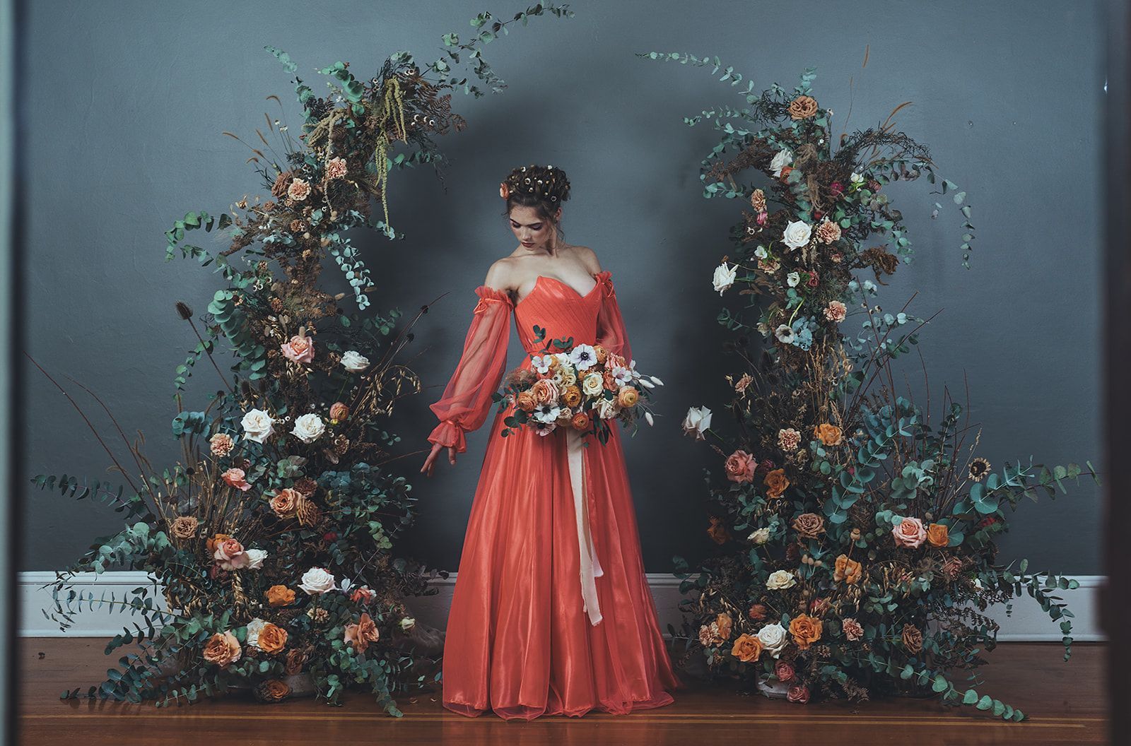 A woman in a red dress is standing in front of a floral arch.