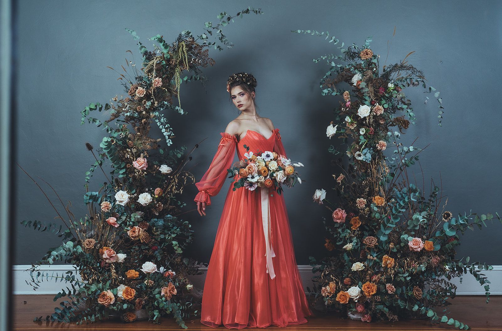 A woman in a red dress is standing in front of a floral arch.