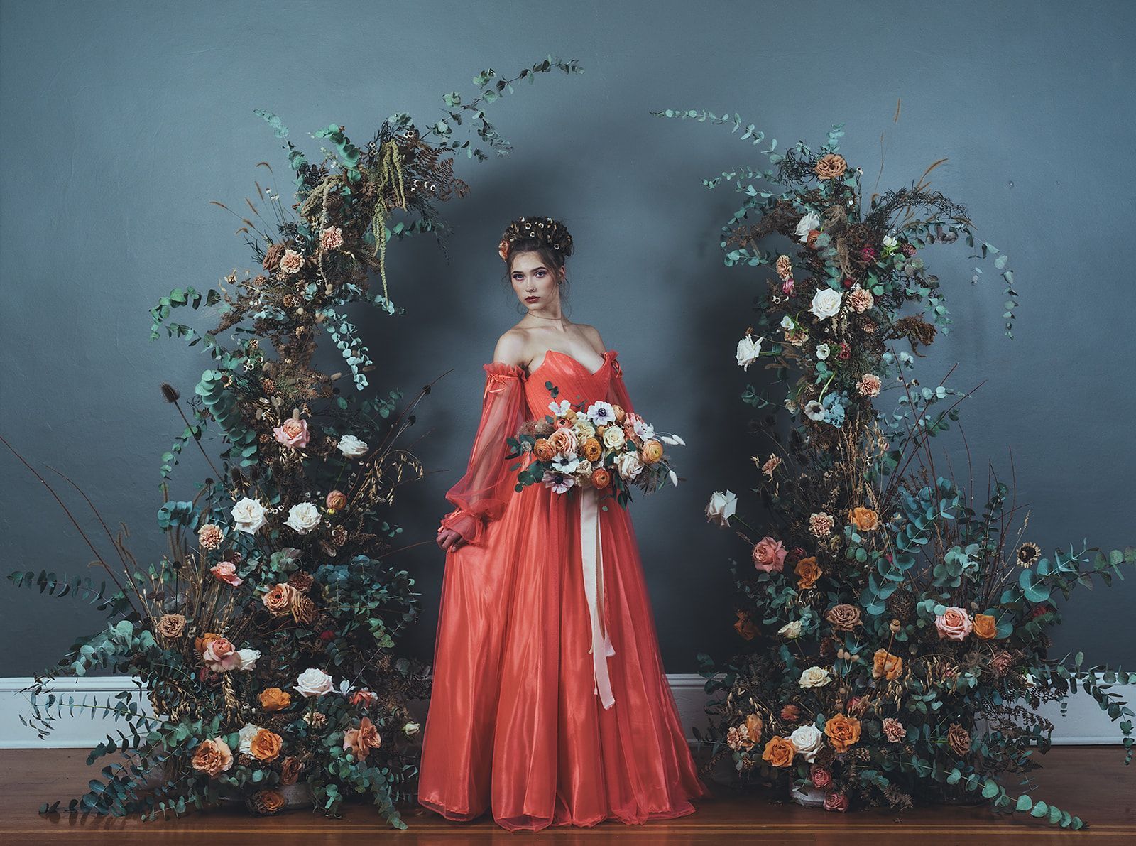 A woman in a red dress is standing in front of a floral arch.