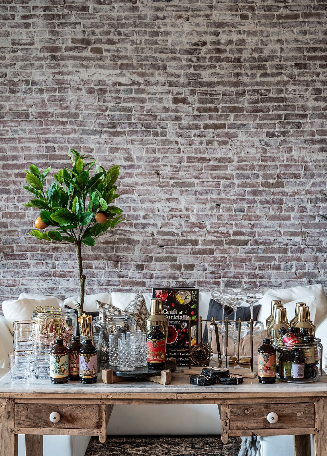A wooden table with bottles and glasses on it in front of a brick wall.