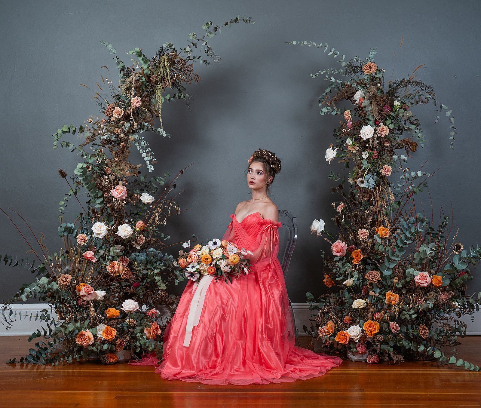 A woman in a red dress is sitting in front of a floral arch.