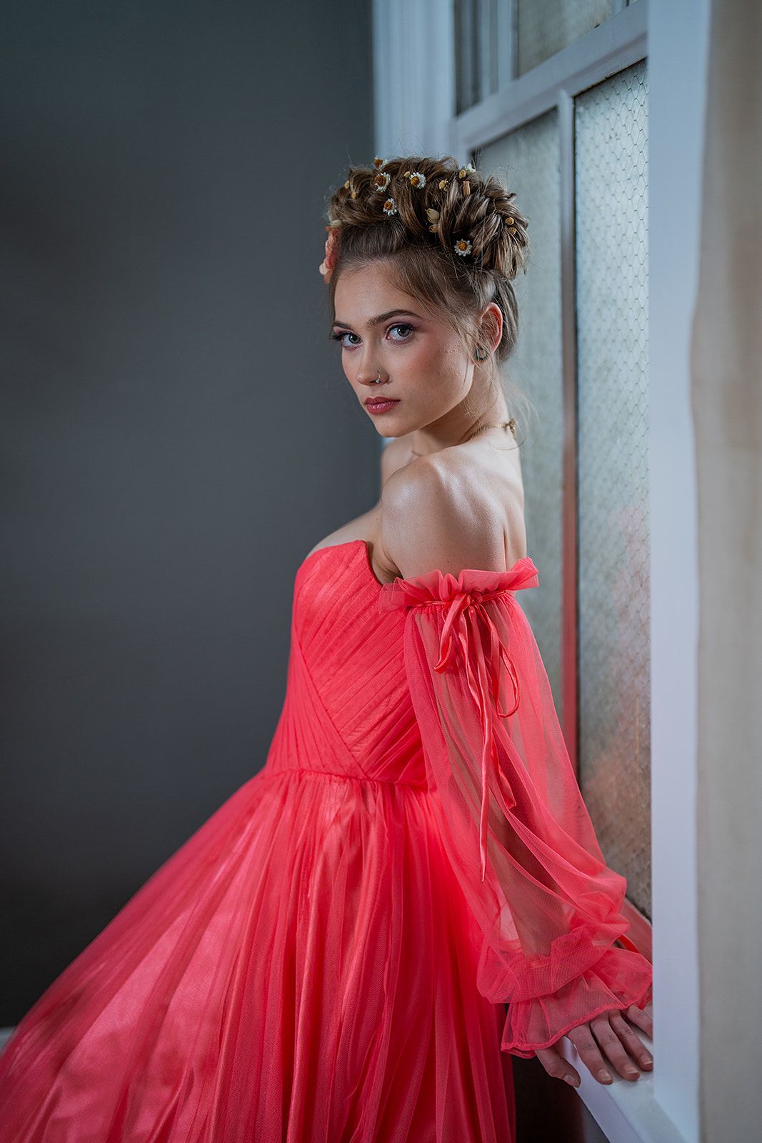 A woman in a red dress is standing next to a window.