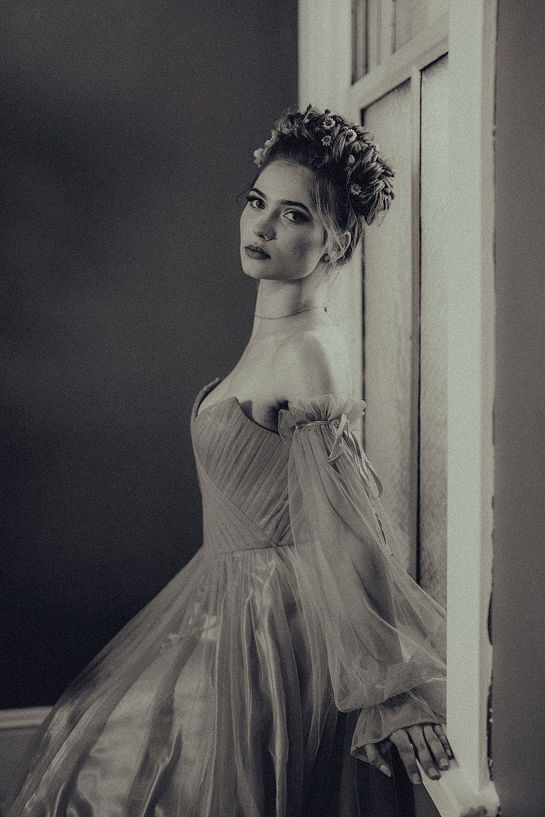 A black and white photo of a woman in a dress standing next to a door.