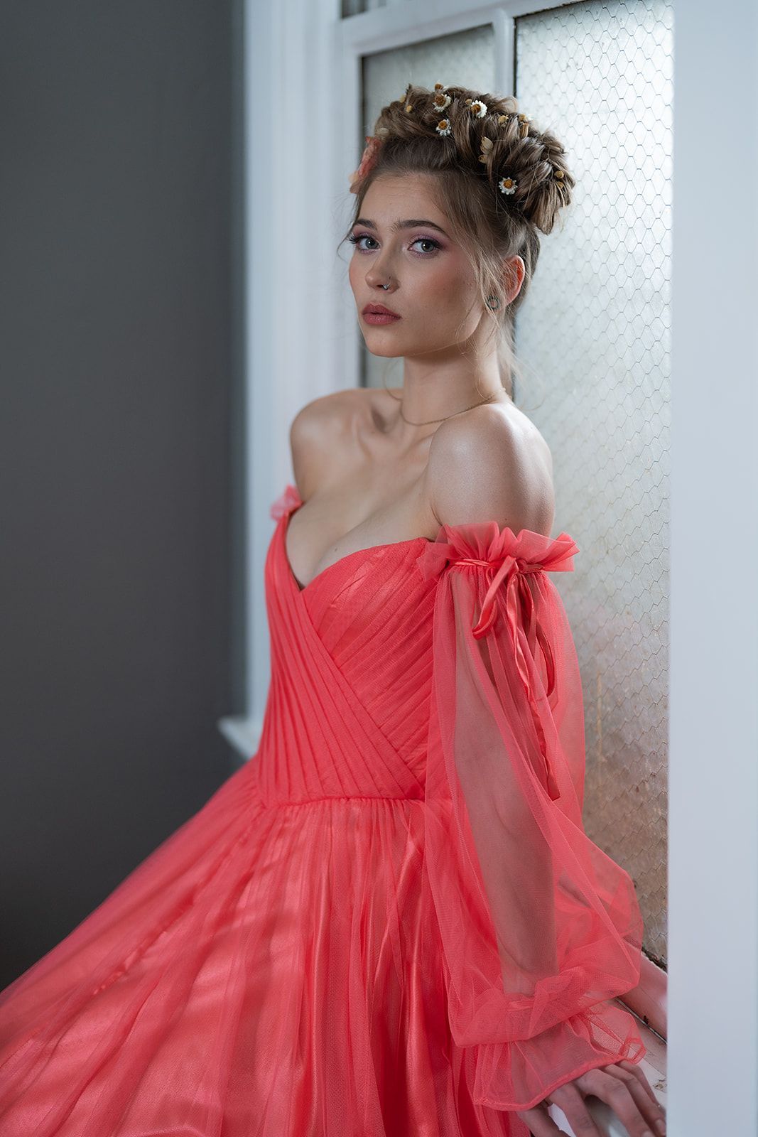 A woman in a red ball gown is standing in front of a window.