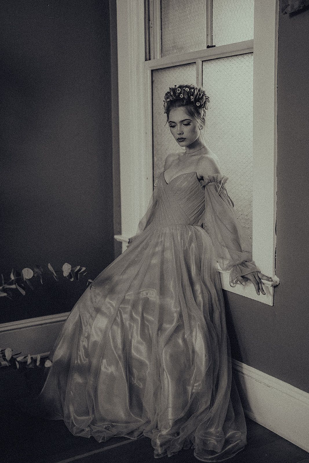 A woman in a long dress is leaning against a window.