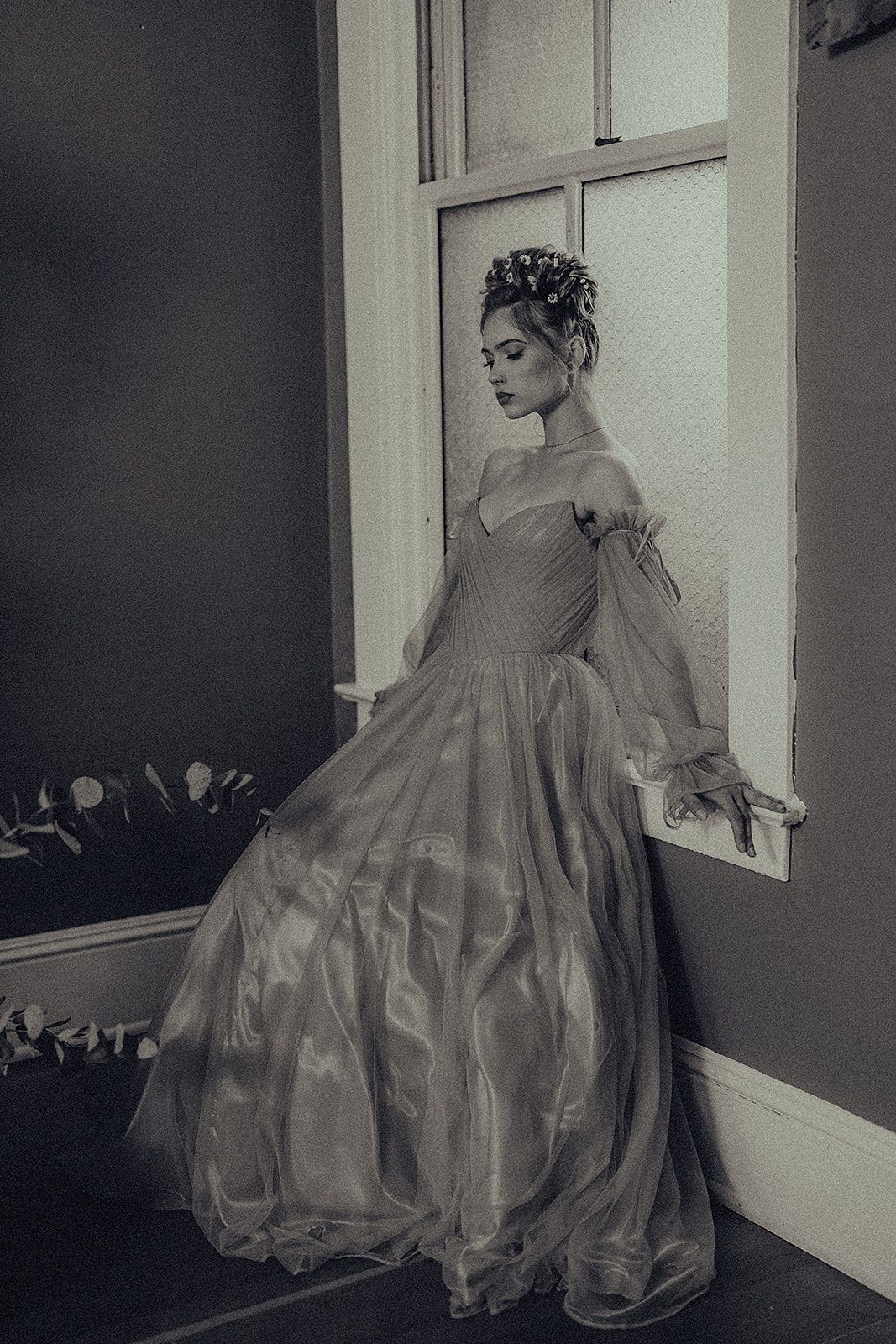 A woman in a long dress is leaning against a window sill.