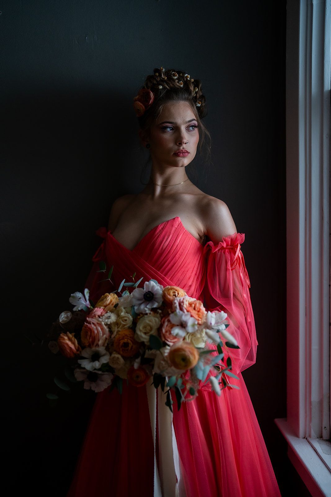 A woman in a red dress is holding a bouquet of flowers and standing in front of a window.