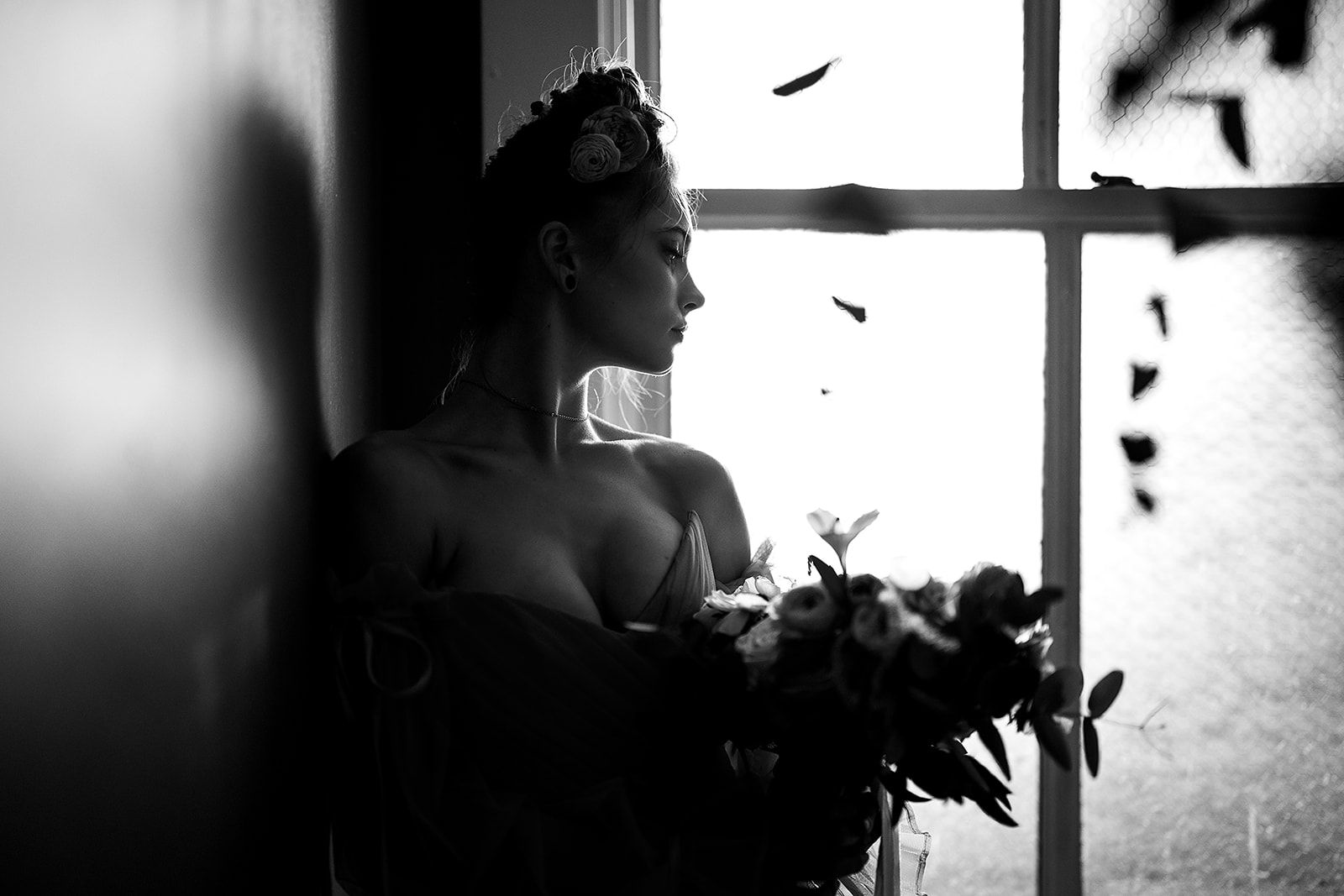 A black and white photo of a woman leaning against a wall holding a bouquet of flowers.