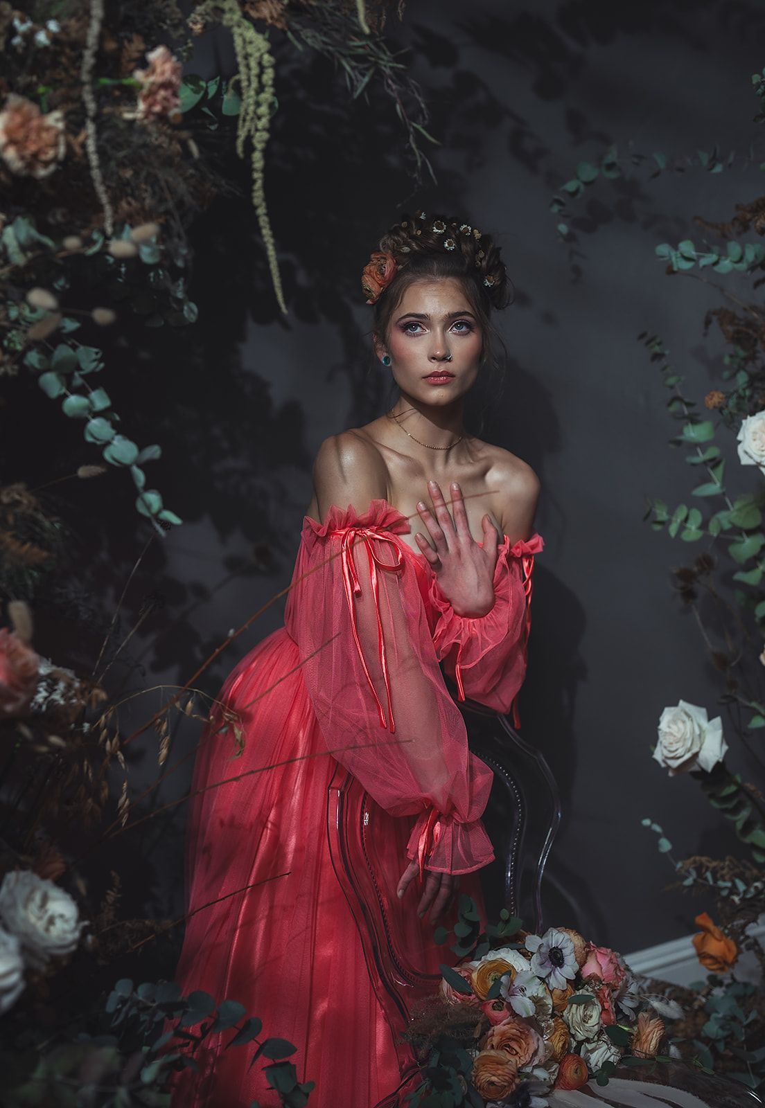 A woman in a red dress is standing in a garden surrounded by flowers.