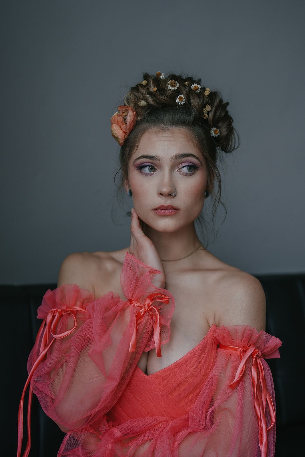 A woman in a pink dress with curlers in her hair is sitting on a couch.