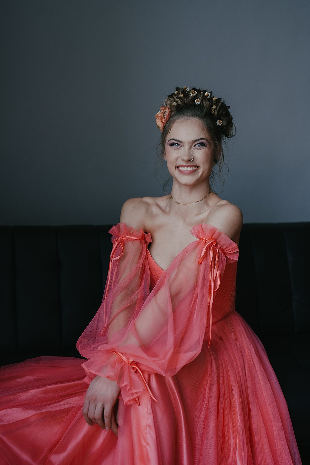 A woman in a pink dress is sitting on a couch and smiling.