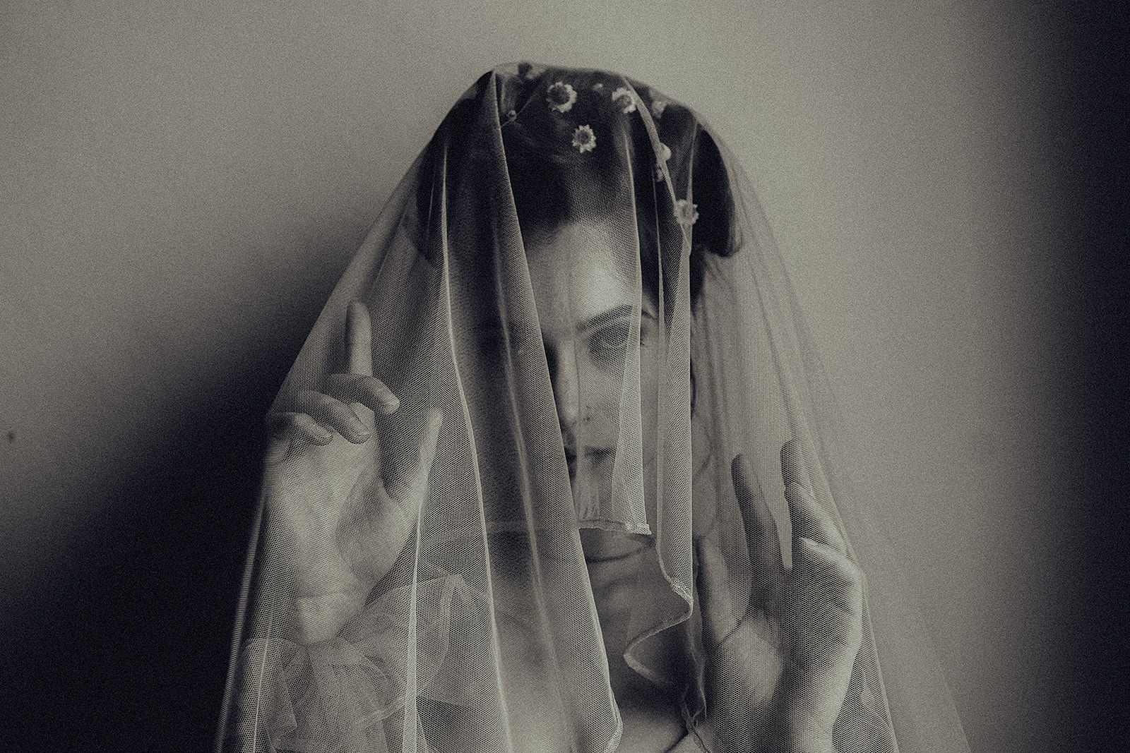 A woman is covering her face with a veil in a black and white photo.