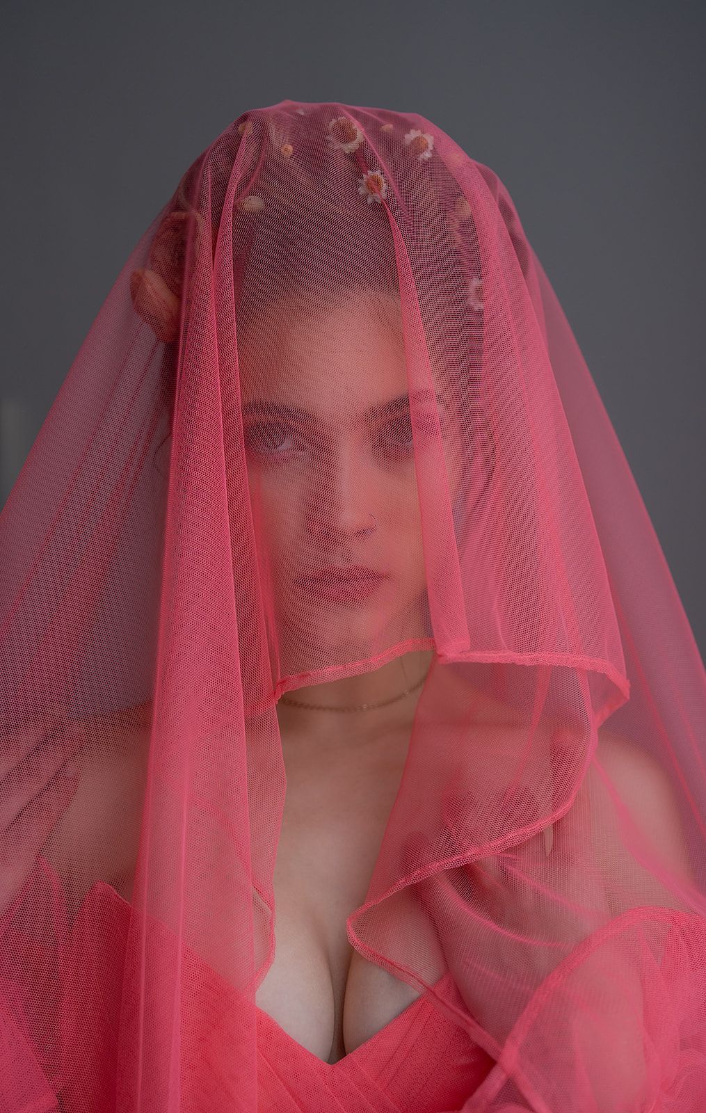A woman is wearing a pink veil over her face.