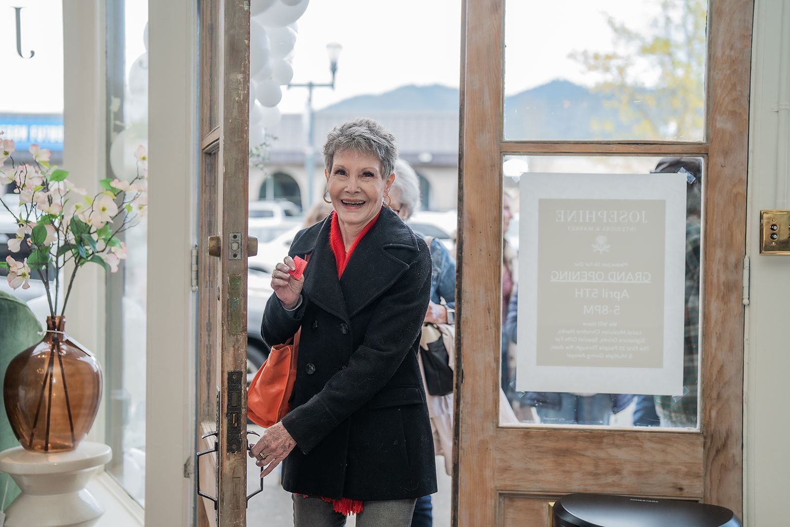 A woman is standing in a doorway holding a purse and smiling.