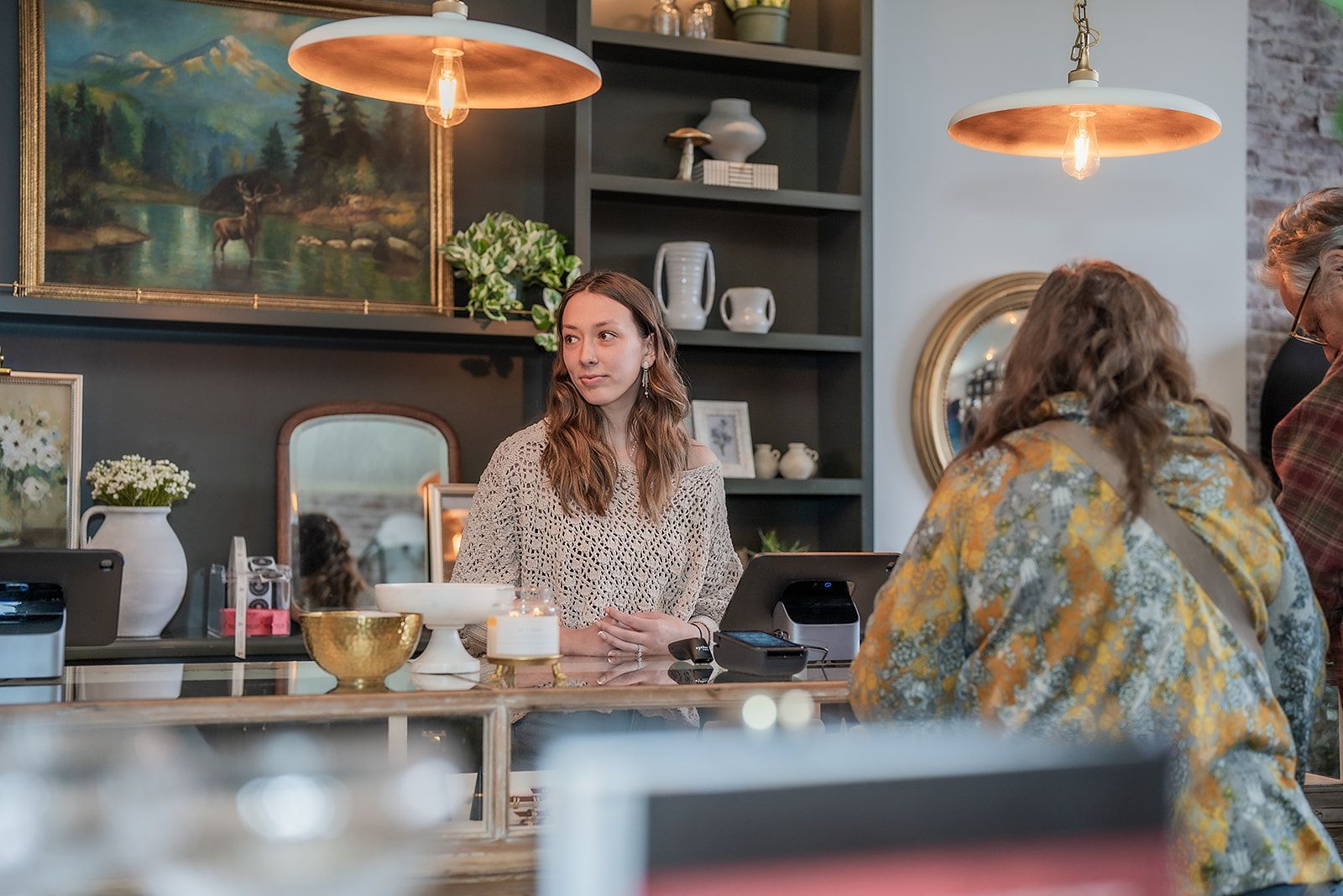 A woman is sitting at a counter in a restaurant talking to a customer.