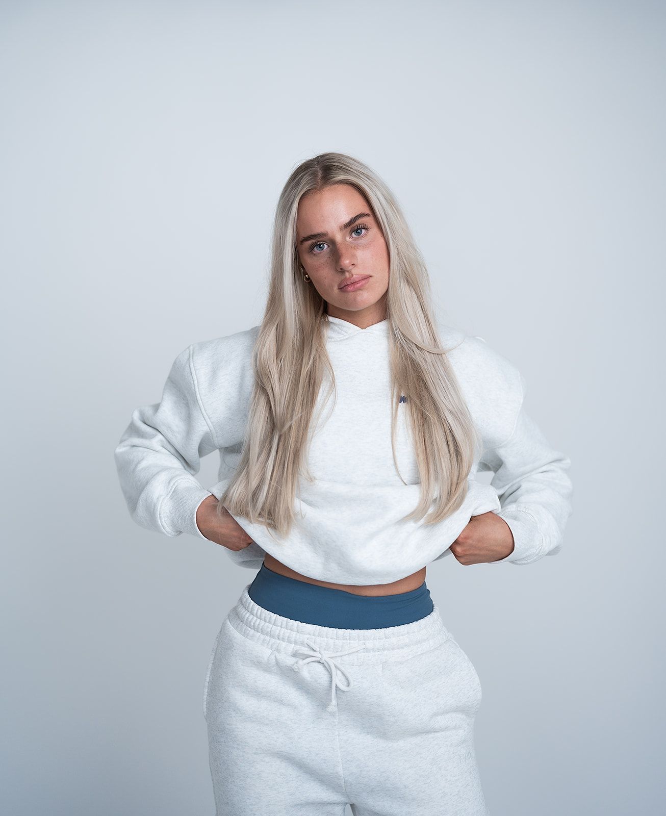 A woman is wearing a white sweatshirt and grey sweatpants.