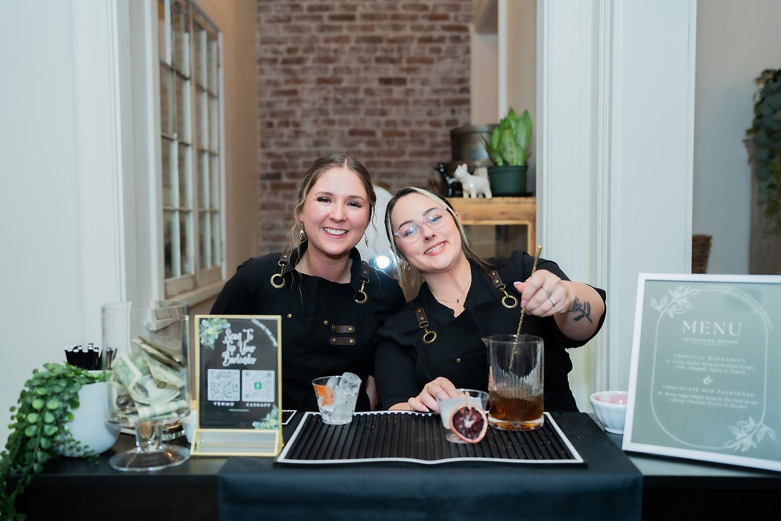Two women are standing next to each other at a table making drinks.