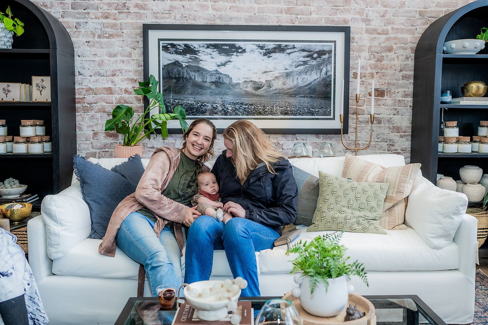 Two women are sitting on a couch holding a baby.