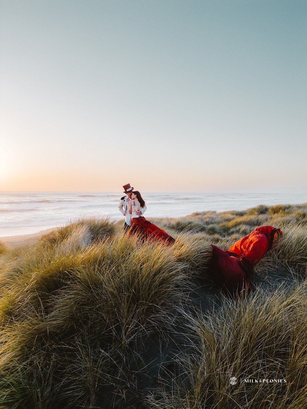 A man and a woman are standing on top of a sand dune near the ocean.