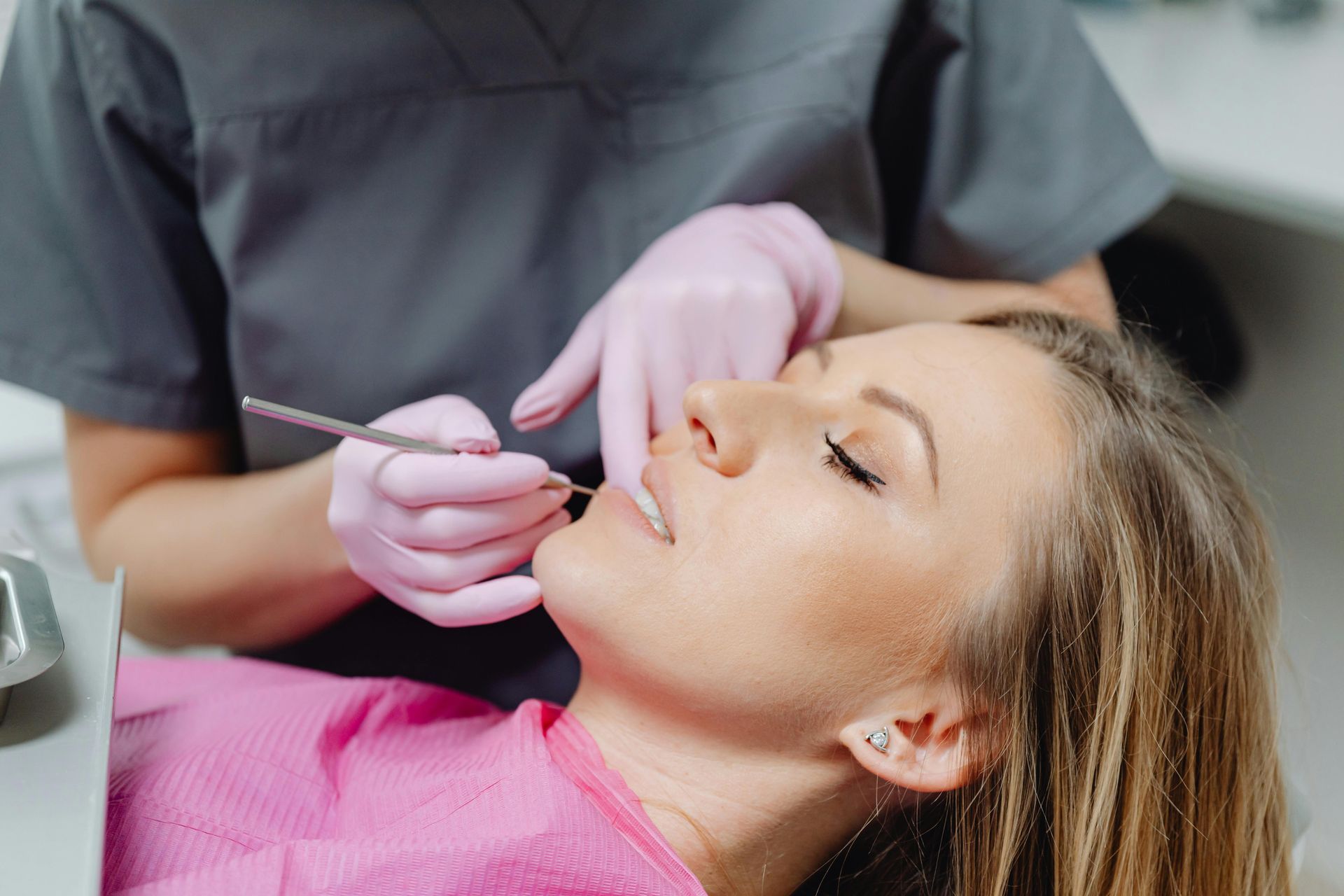 Woman at dentist, mouth open, being examined. Dentist wearing pink gloves, using dental tool.