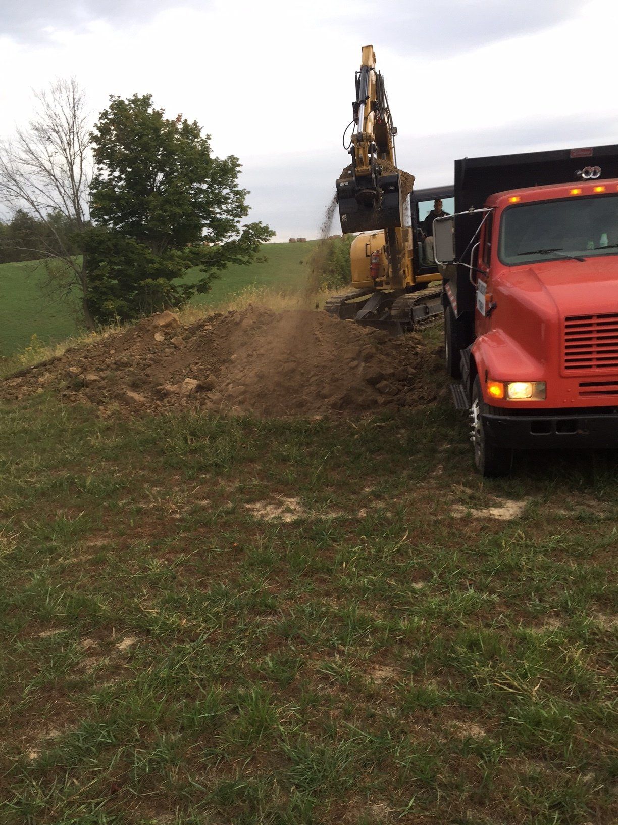 A red dump truck is parked in a grassy field next to an excavator.