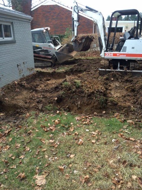 A bulldozer is digging a hole in the ground in front of a house.