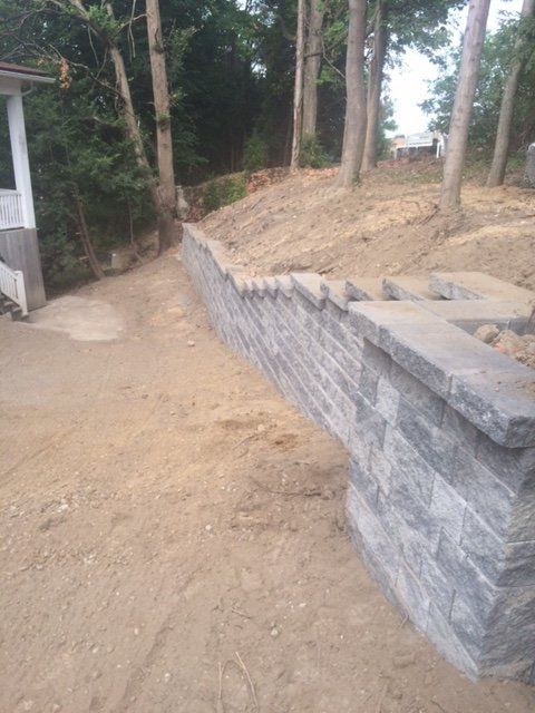A stone wall is sitting on top of a dirt hill next to a house.