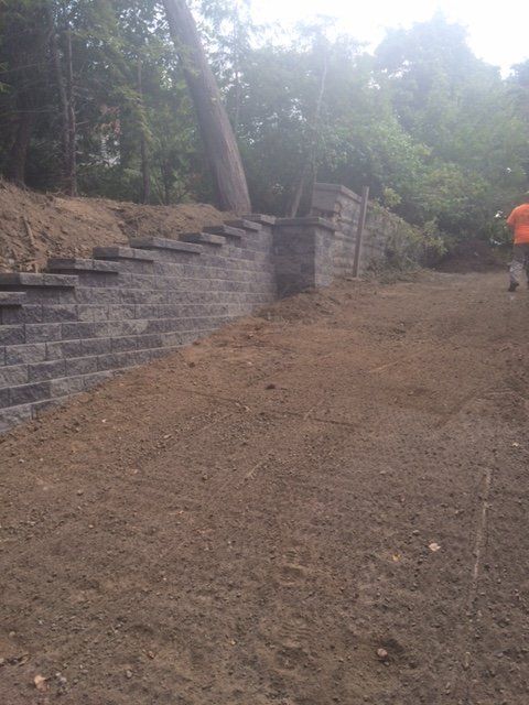 A man is walking down a dirt path next to a brick wall.