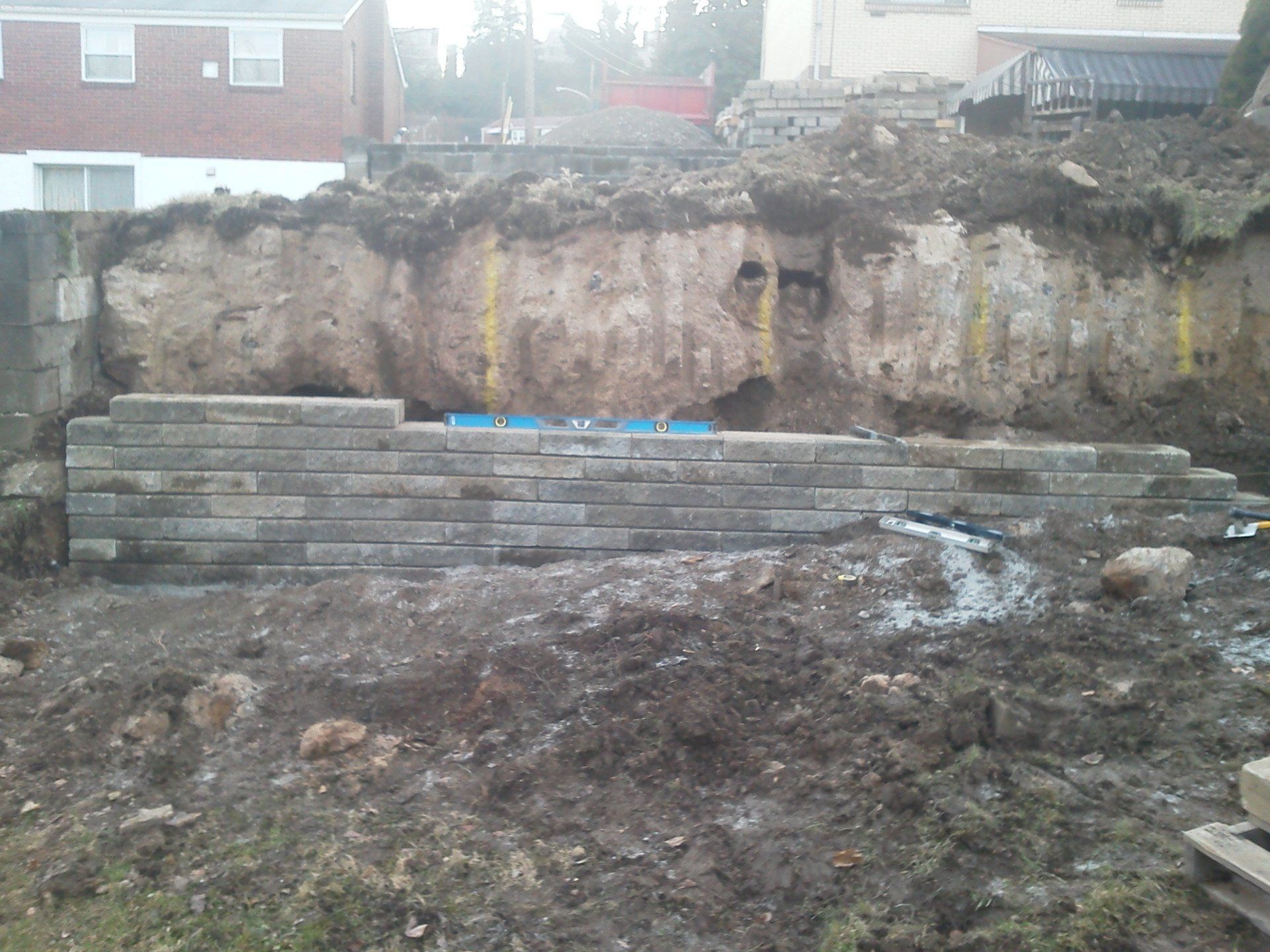 A brick wall is being built in the dirt in front of a house