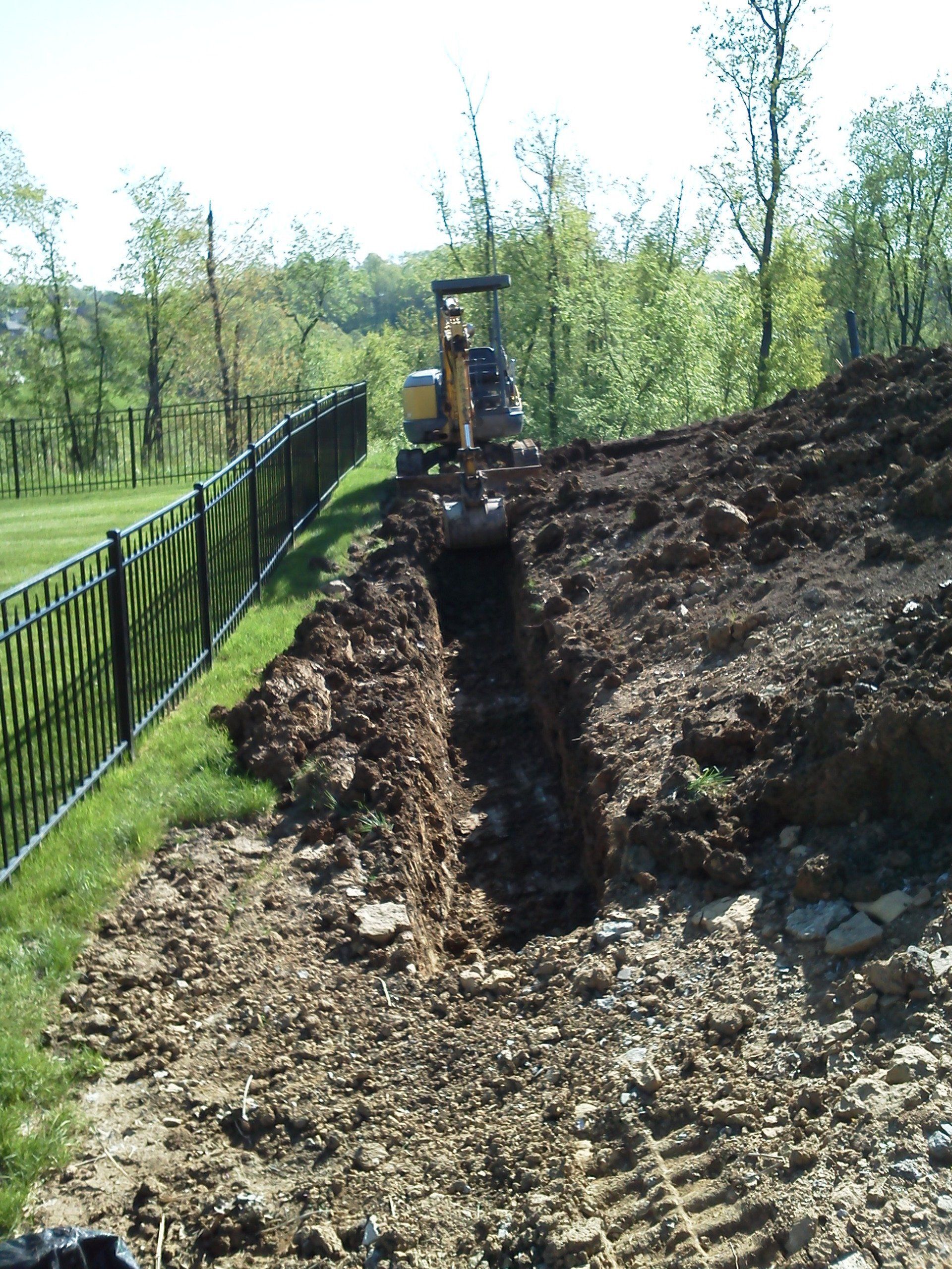 A bulldozer is digging a hole in the ground near a fence
