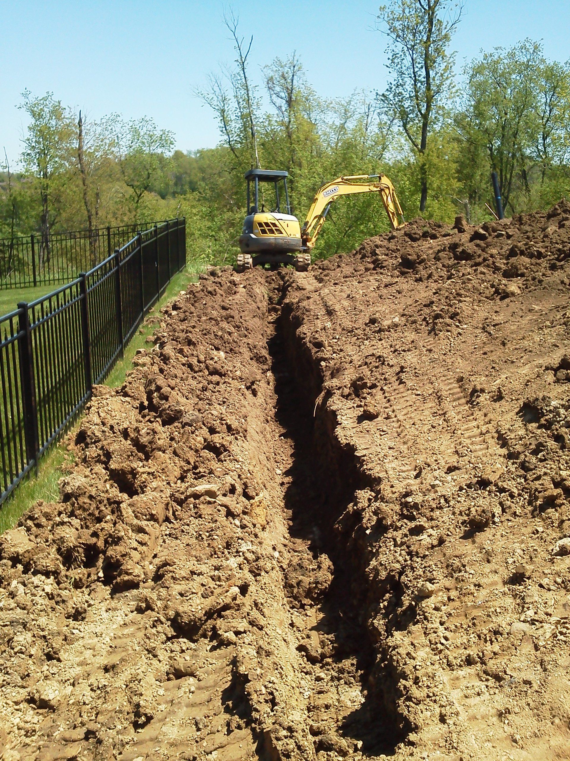A yellow excavator is digging a trench in the dirt.