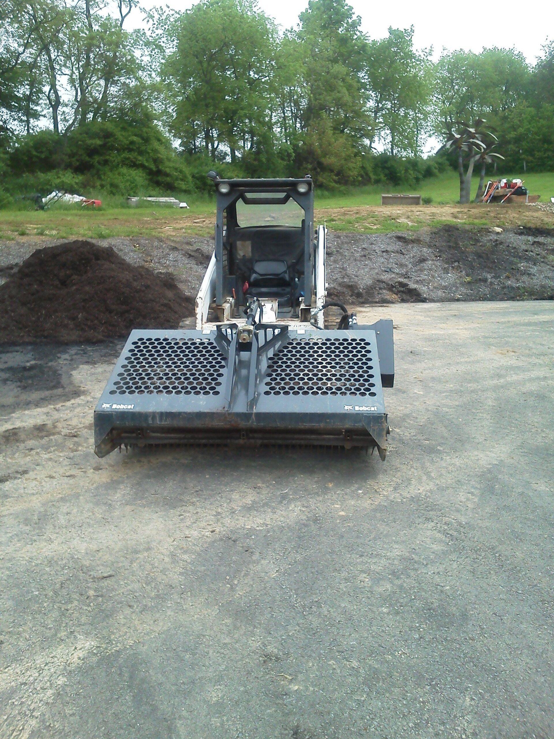 A skid steer is parked on a dirt road next to a pile of dirt