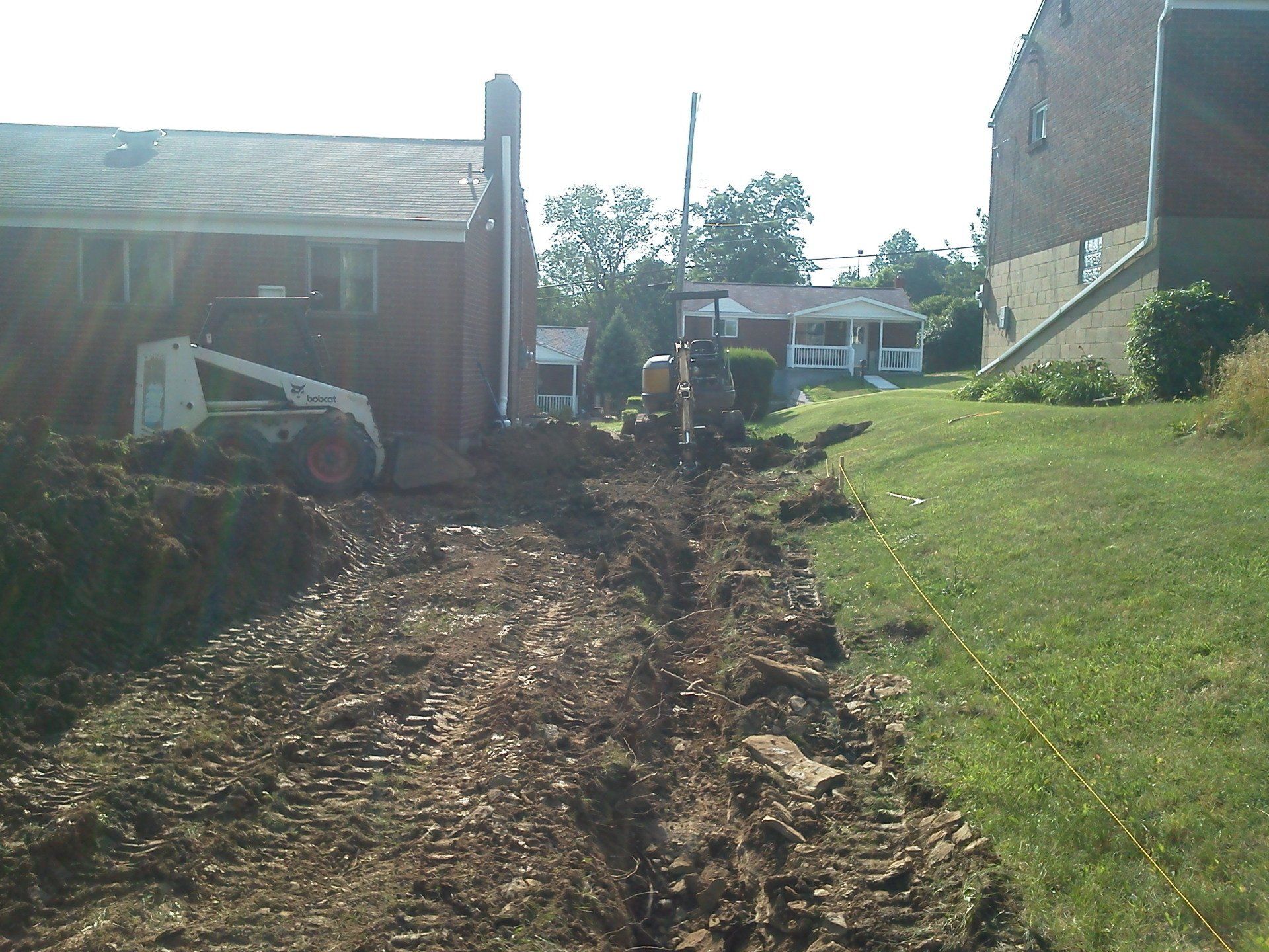 A bobcat is driving down a dirt road in front of a house