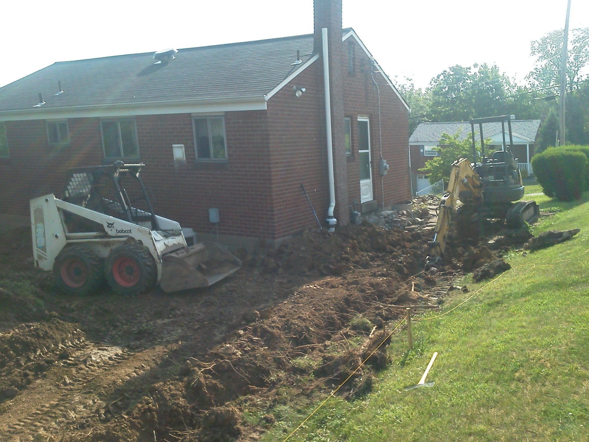 A bobcat is digging a hole in front of a brick house