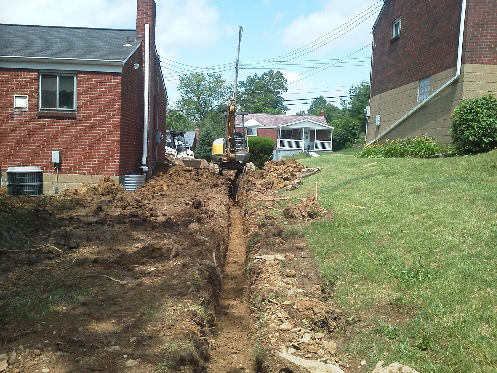 An excavator is digging a trench in front of a brick house
