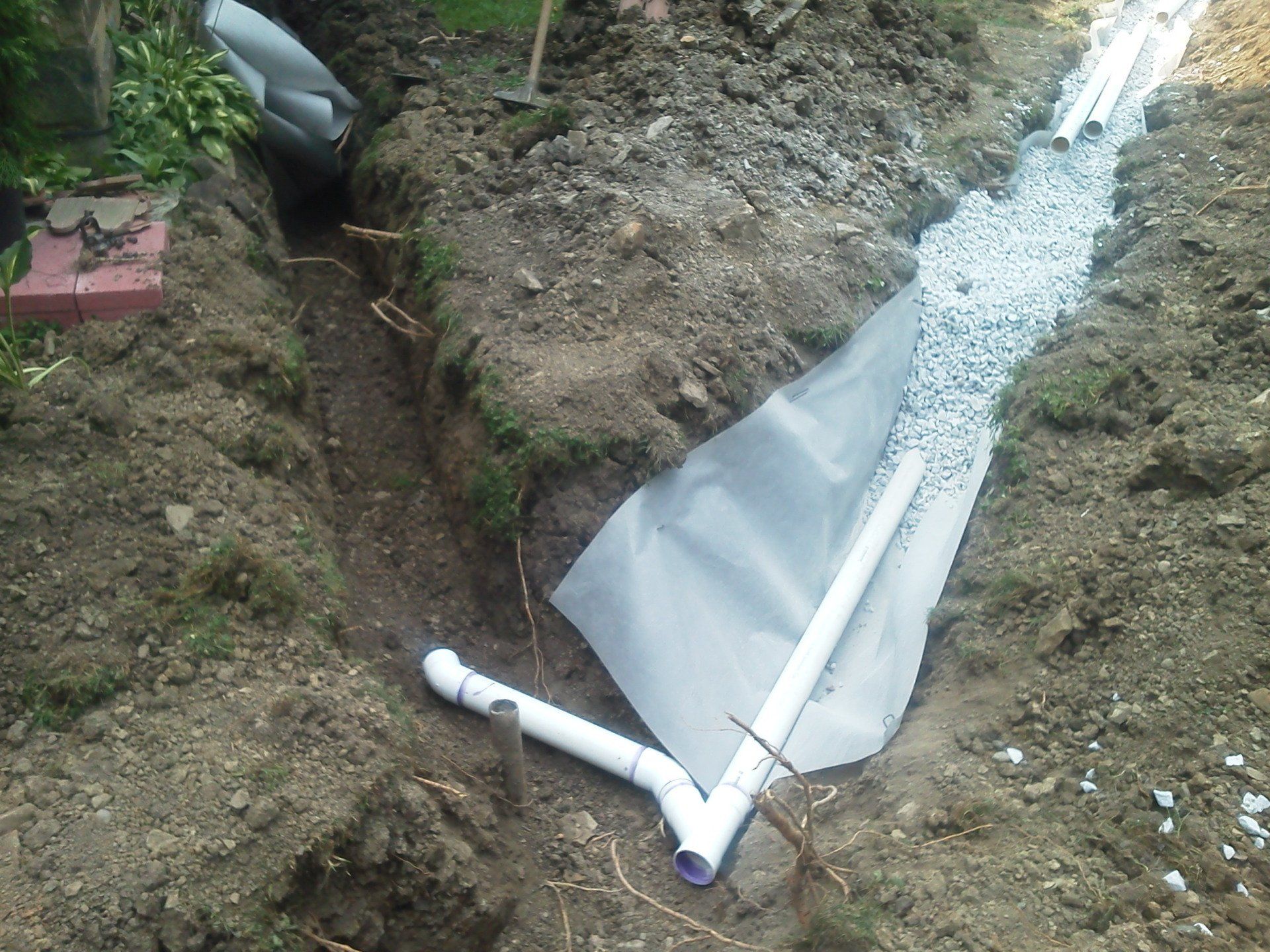 A white pipe is laying in the dirt next to a drain