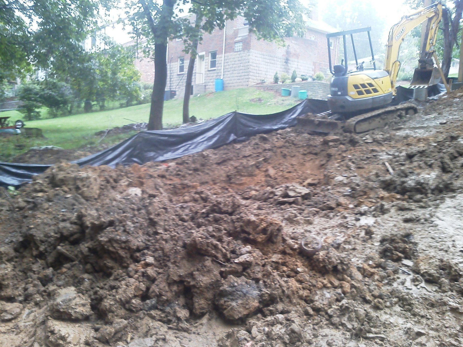 A yellow excavator is working on a pile of dirt in front of a house
