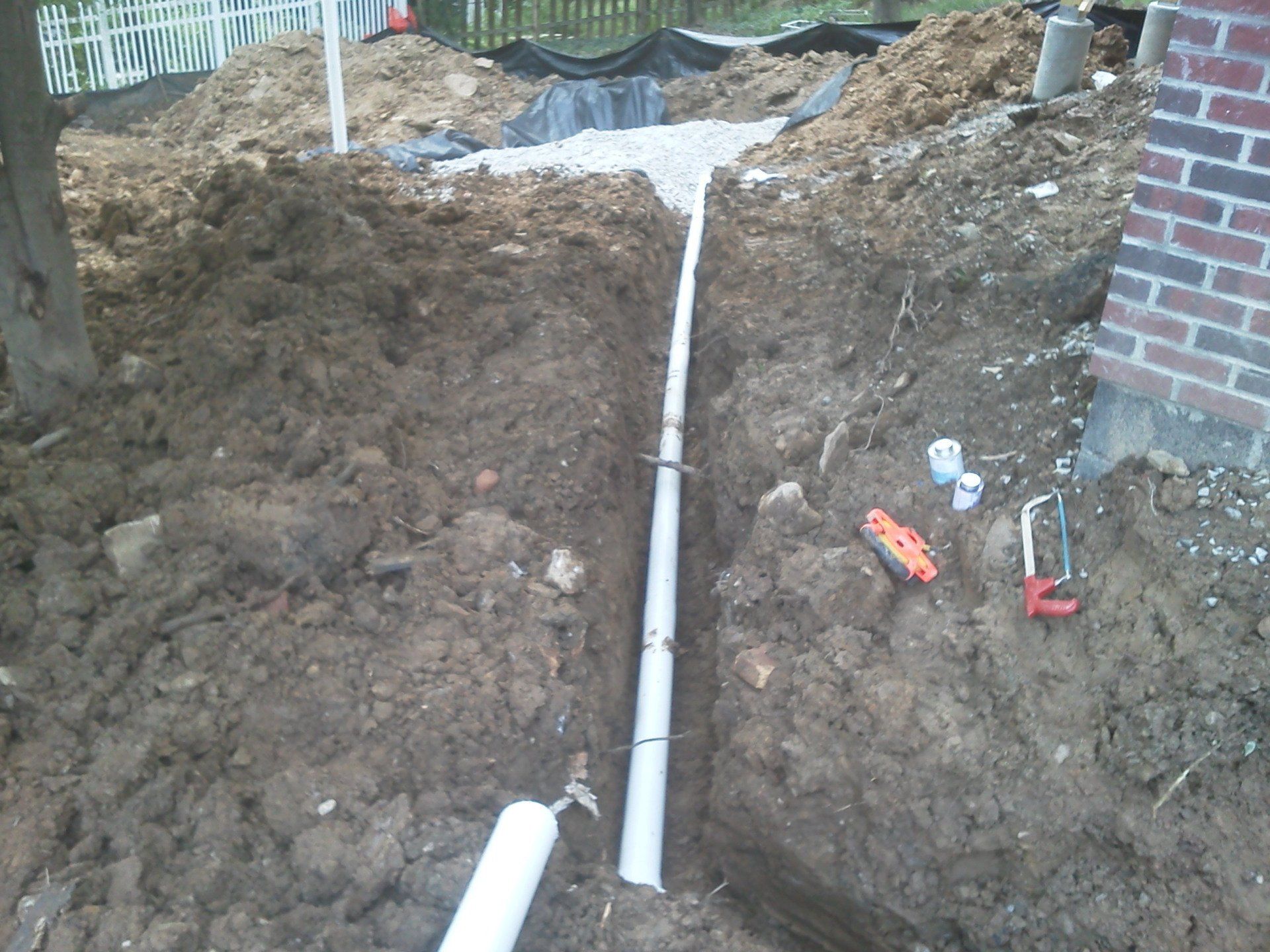 A white pipe is laying in the dirt next to a brick wall