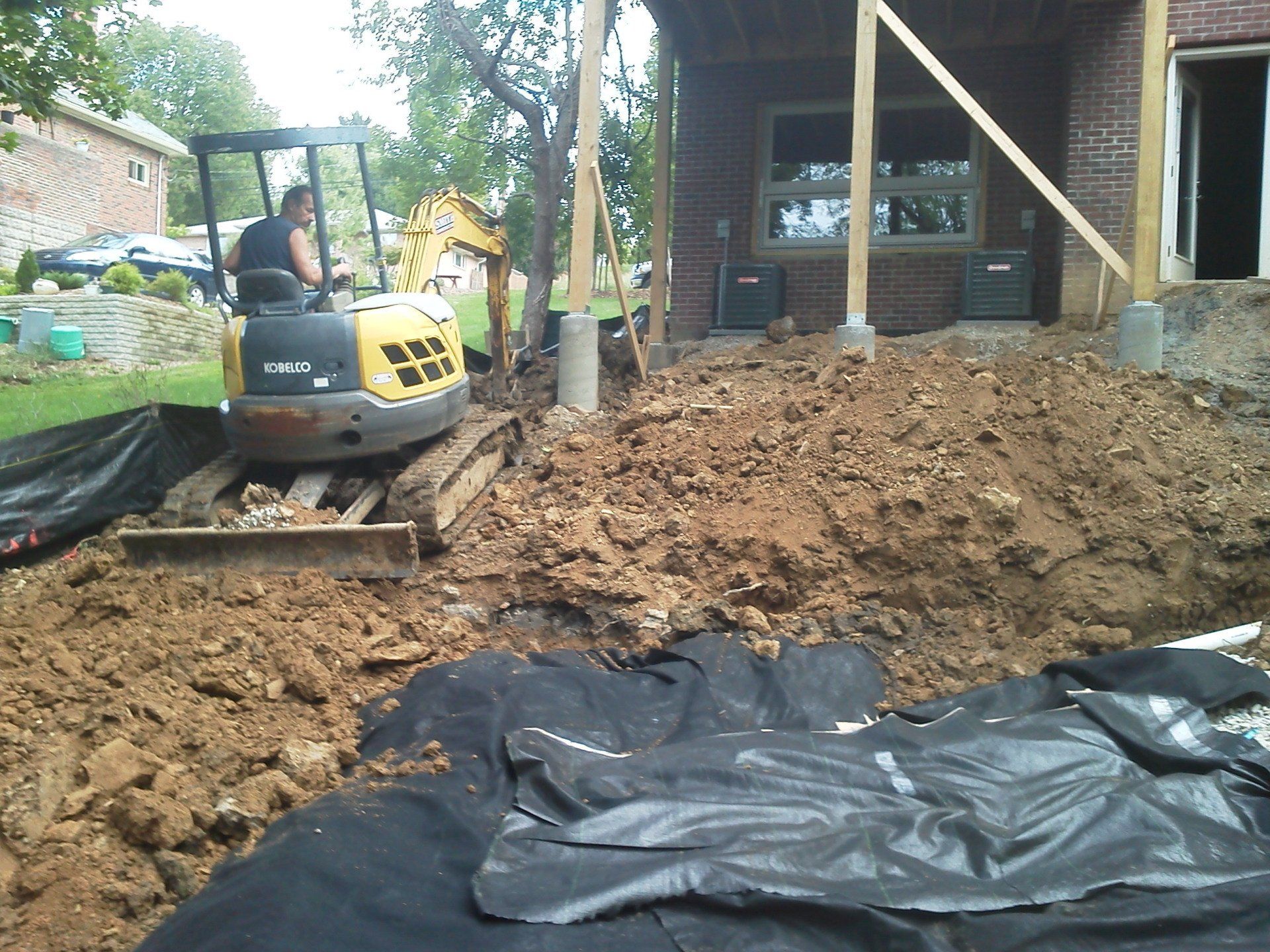 A man is driving a bulldozer in the dirt in front of a brick house
