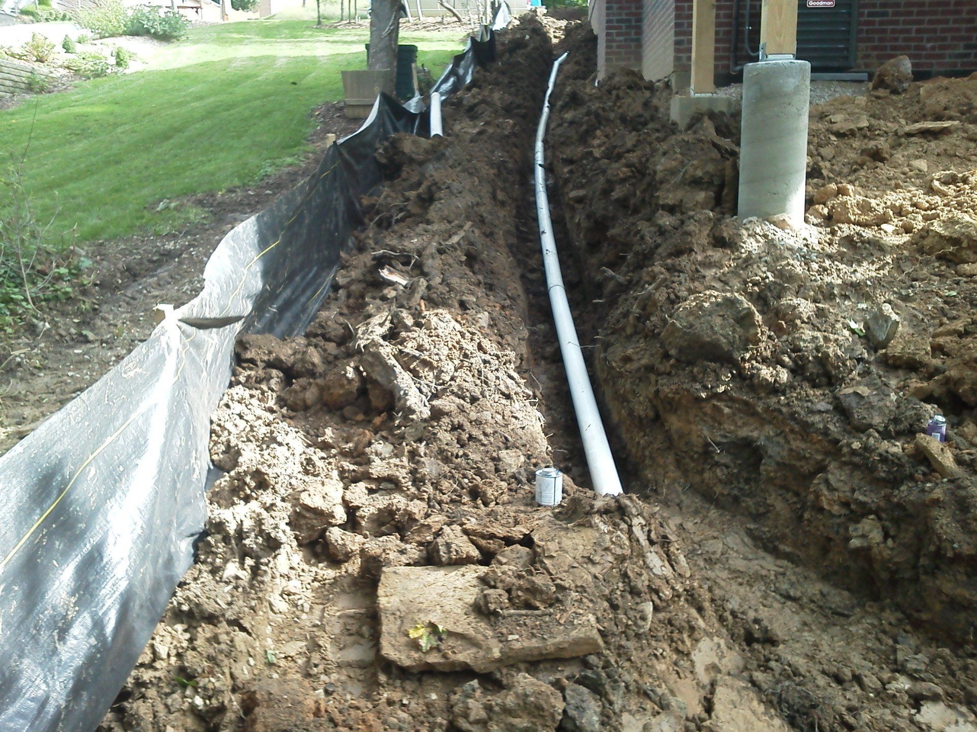 A drain pipe is being installed in the dirt in front of a house.