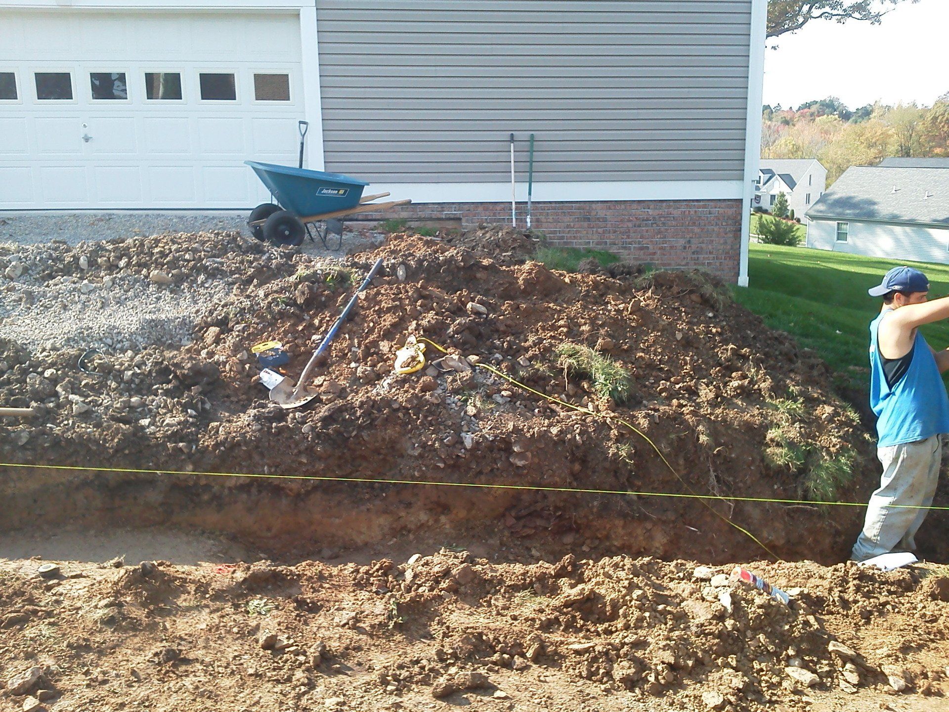 A man is measuring a hole in the ground in front of a house