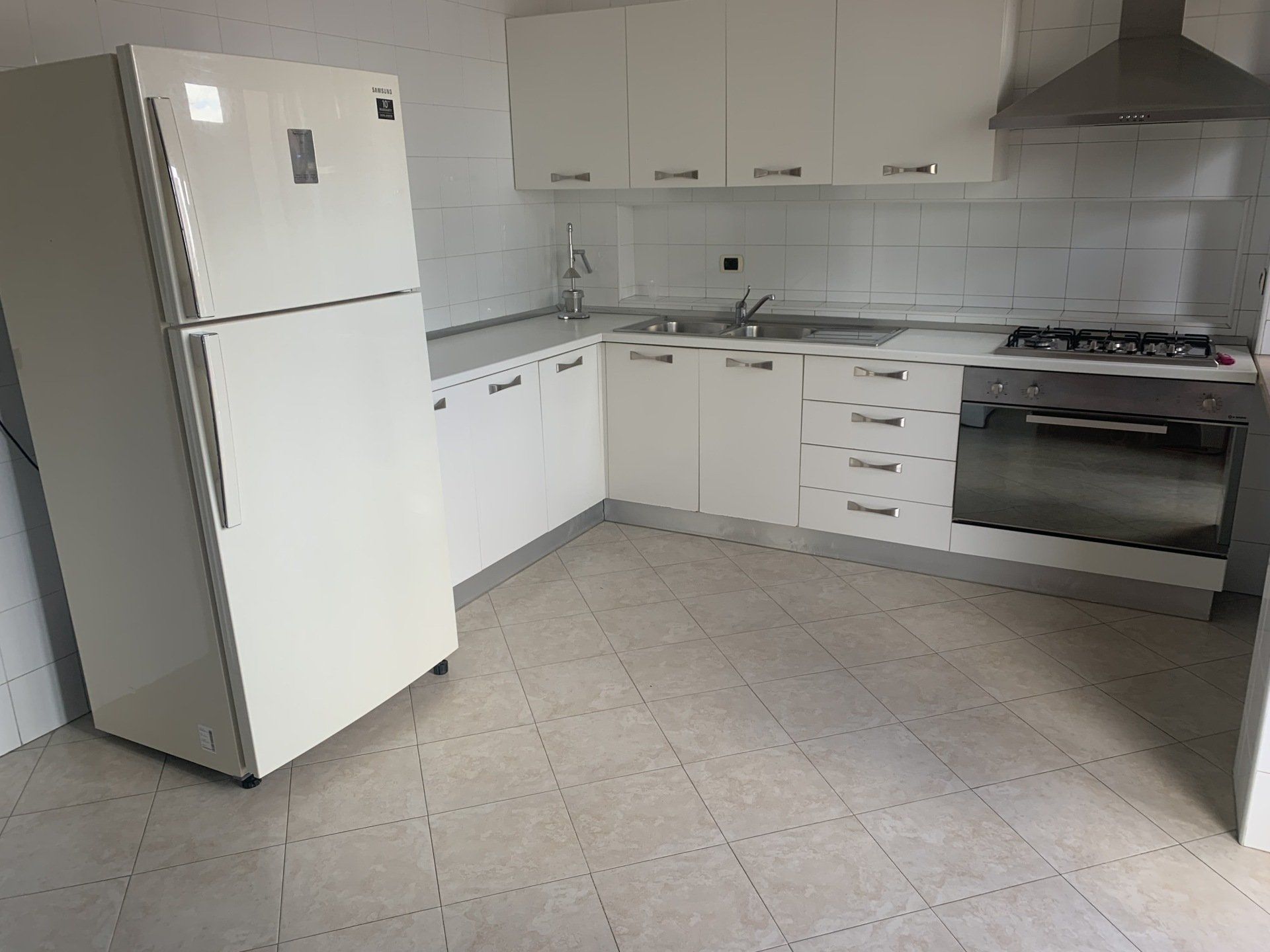 Una cucina con mobili bianchi, un frigorifero e una stufa