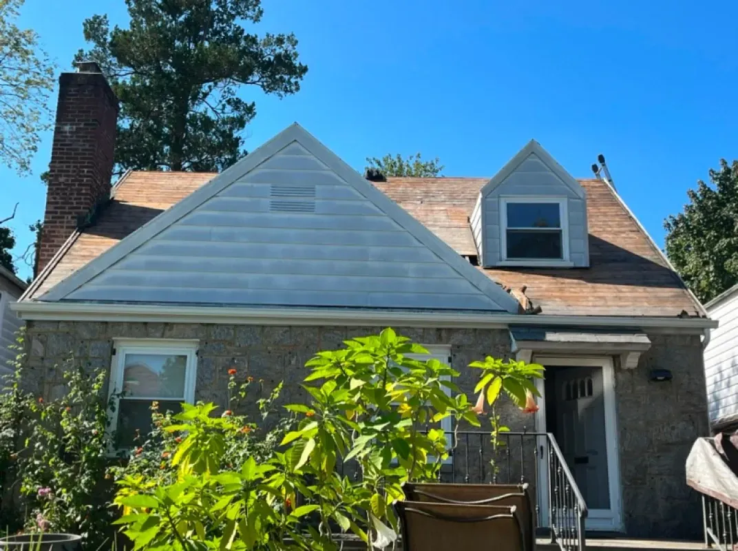 A stone house with a large brick chimney, a white-sided gable, and a small dormer under a bright blue sky.