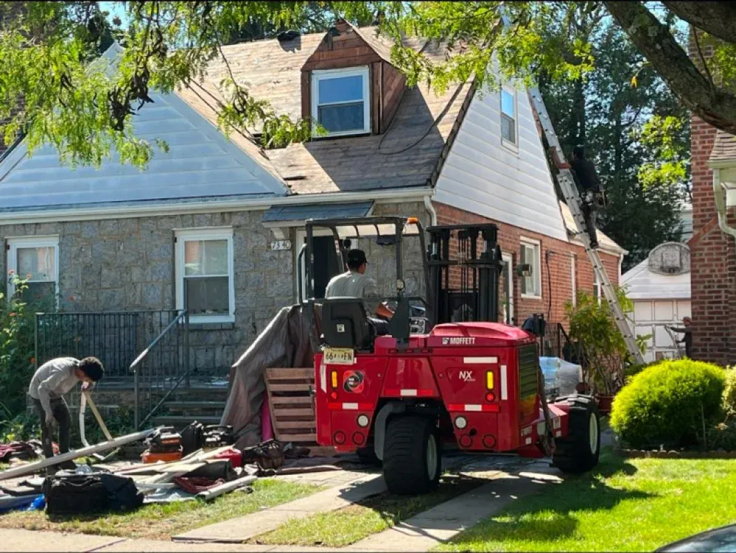 Workers renovate a residential home roof while a red forklift sits in the driveway with materials.