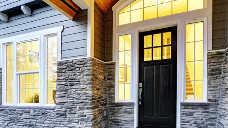 A dark-colored front door with a glass transom and side windows, framed by stone veneer siding and light-colored trim.
