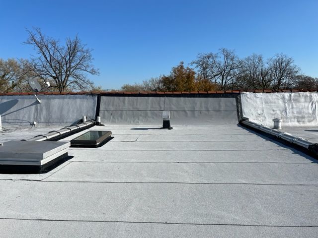 A wide-angle view of a flat commercial roof with gray roofing membrane, several skylights, and a clear blue sky.