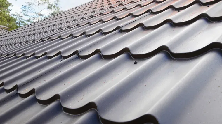 A close-up, angled view of a dark brown, corrugated metal roof with a repeating wave pattern under natural light.